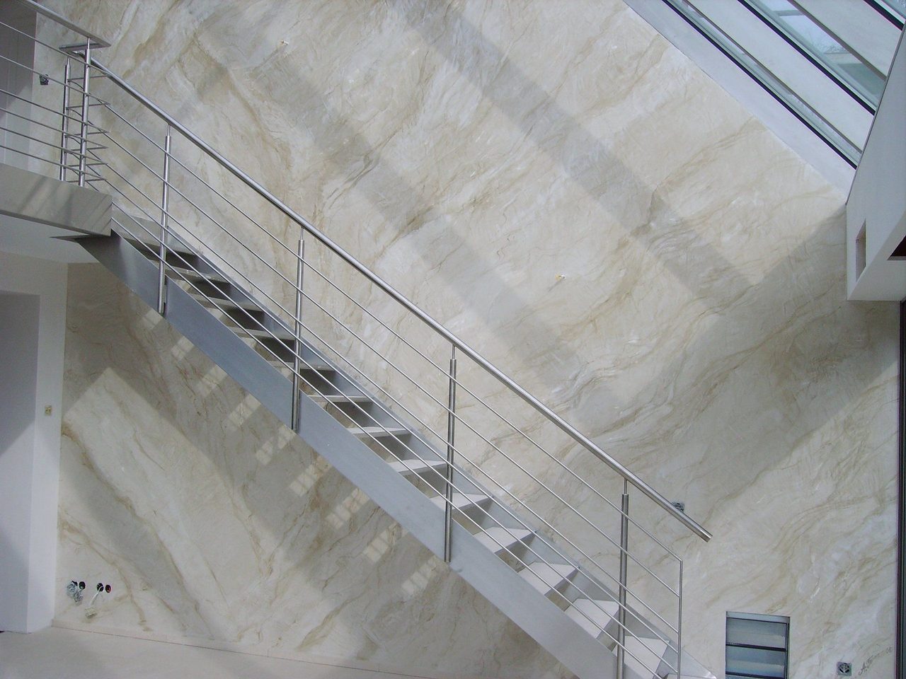 Treppe mit Edelstahlgeländer vor einer weißen Marmorlasur